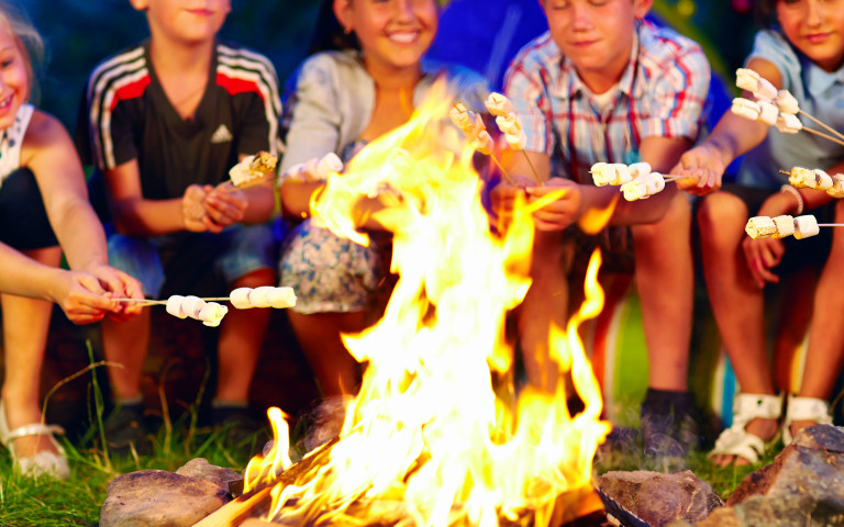 enfants qui réchauffent leurs marshmallows dans un feu de camp