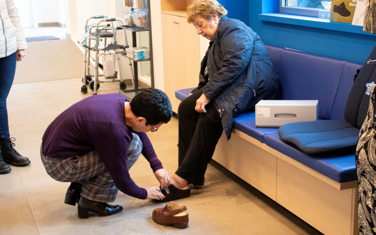 Medewerker van de winkel van Zorgboetiek in Aalst helpt een klant die schoenen past.