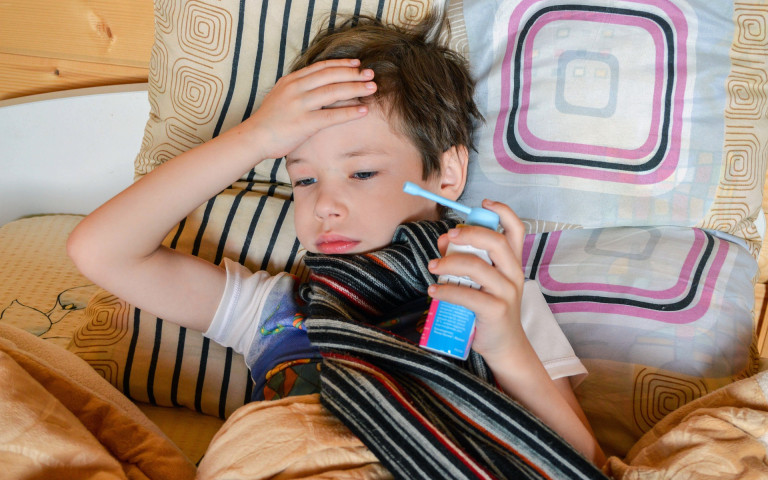 enfant malade dans son lit qui tient un spray médicament dans sa main