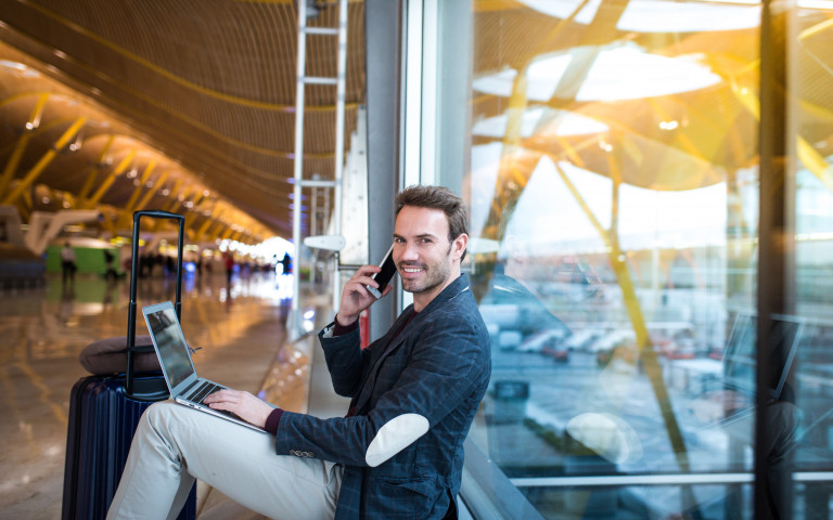 man met smartphone werkt op laptop in luchthaven