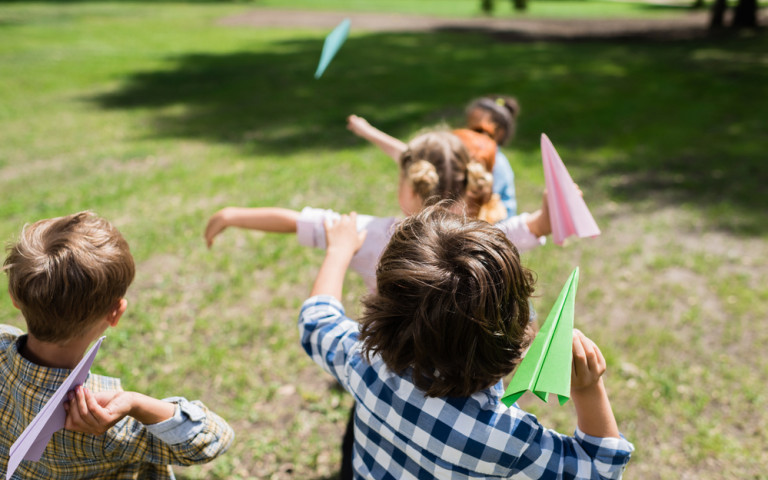 Kinderen spelen buiten en gooien met papieren vliegtuigjes