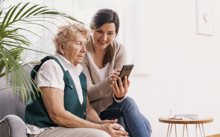 oude vrouw en jonge vrouw zitten samen in de zetel en kijken naar smartphone