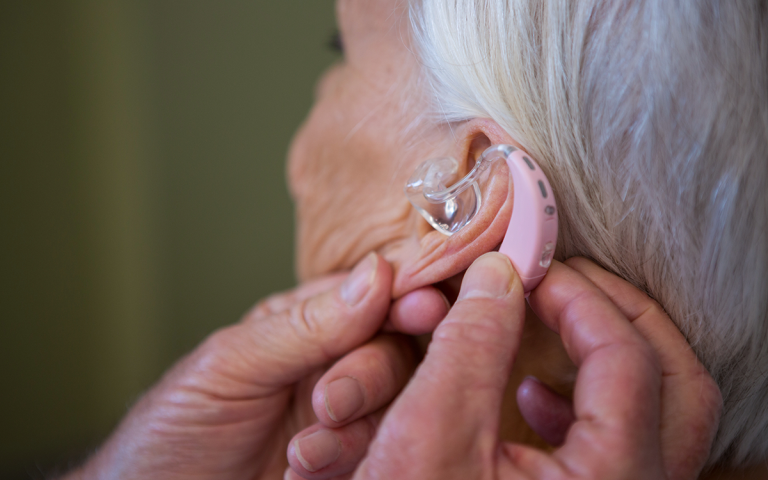 oude dame met gehoorproblemen, iemand die haar helpt met het hoorapparaat