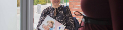 Vroedvrouw aan de voordeur bij een zwangere vrouw thuis.