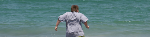 Jongen met overgewicht loopt de zee in