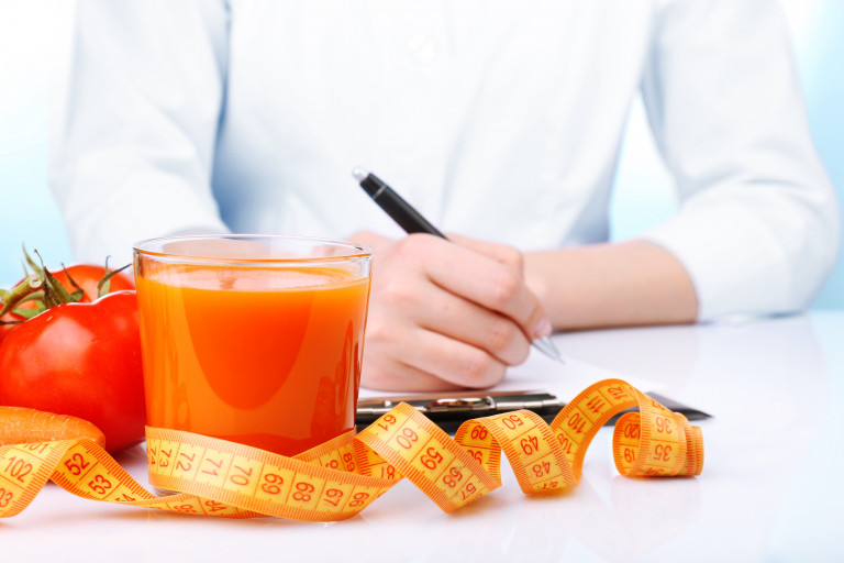 Diététicienne qui élabore un plan diététique avec un jus de tomates et un mètre ruban