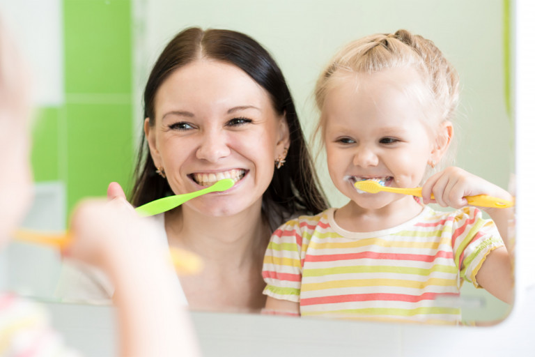 Moeder en dochter poetsen samen hun tanden voor de spiegel