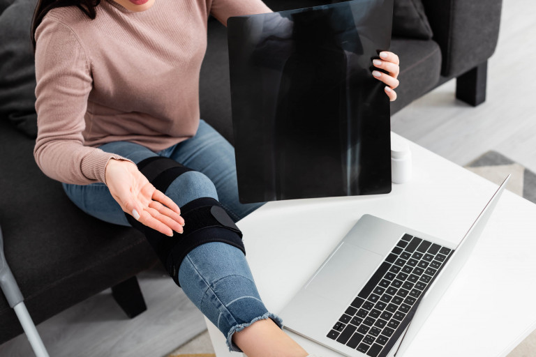 vrouw met brace aan knie werkt op laptop