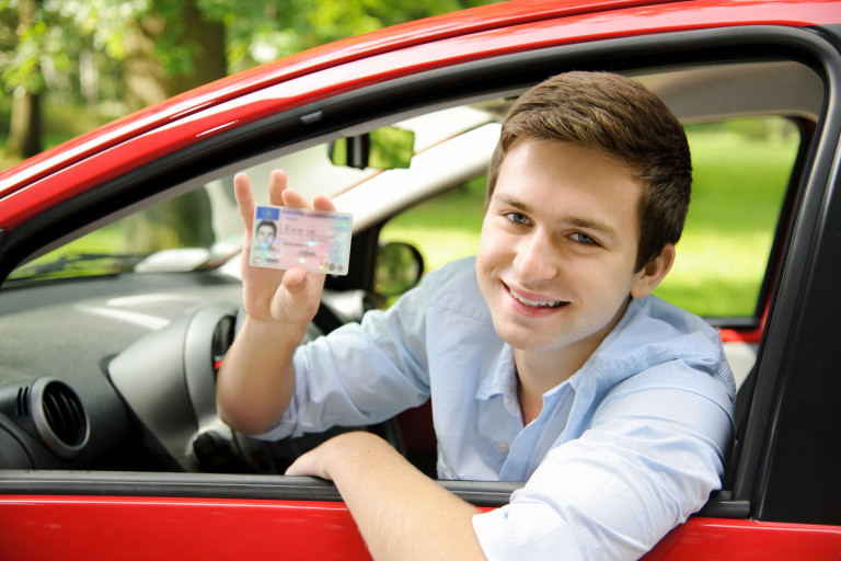 Jeune homme qui est dans une voiture et montre son nouveau permis de conduire