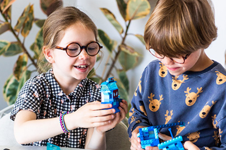 Twee kinderen met bril spelen met legoblokken